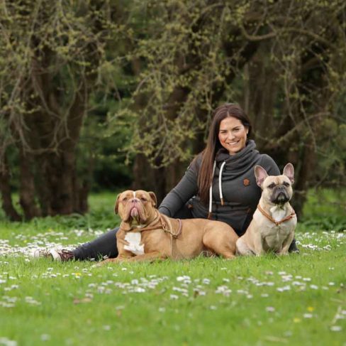 Hundetrainerin liegt mit zwei Hunden auf der Wiese